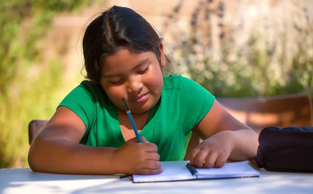 student writing on a table outside