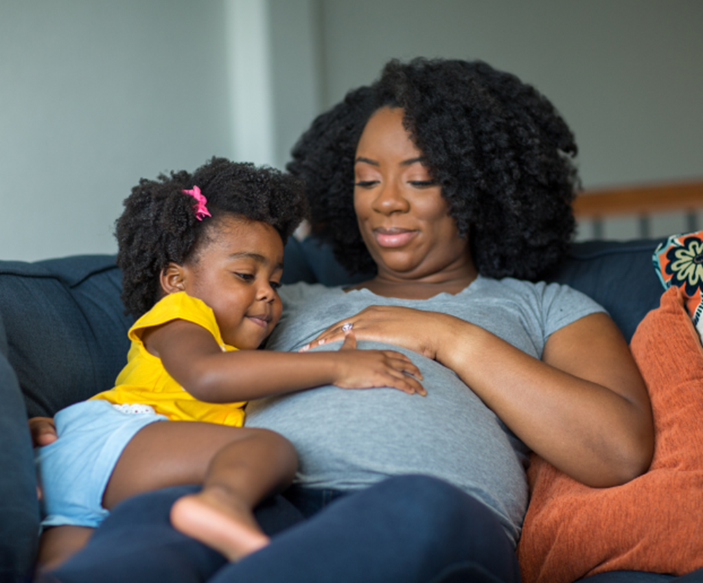 Expecting mother sits on the couch with daughter