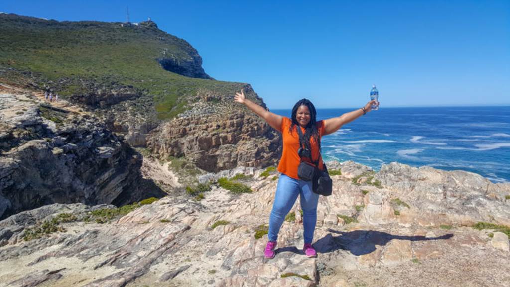 Woman stands on ocean side cliff excitedly