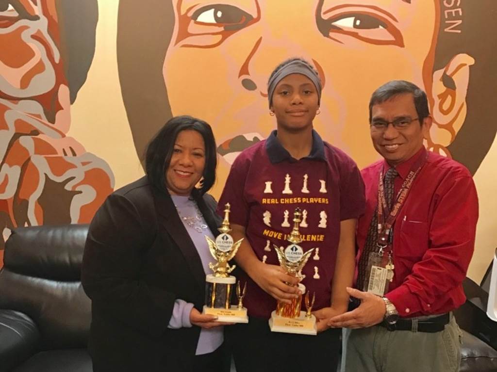 A student and two faculty stand with trophies in hand