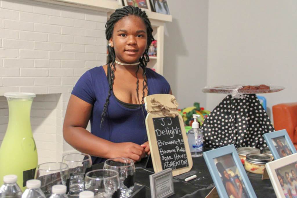 A girl stands behind a table of refreshments