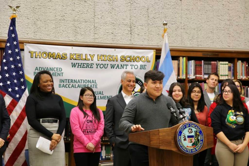 Students stand behind a student that is standing at a podium