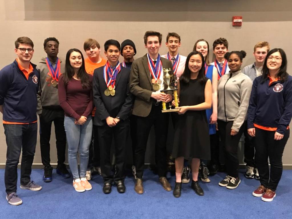 A team of students stand behind a trophy