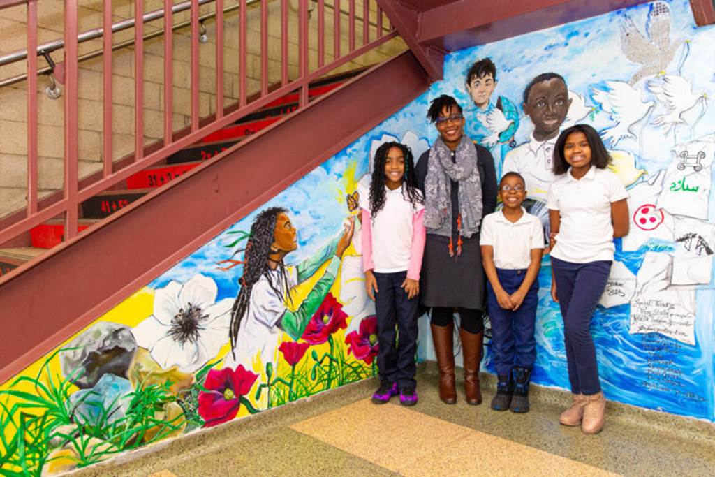 Students standing in front of a painting on a stairway