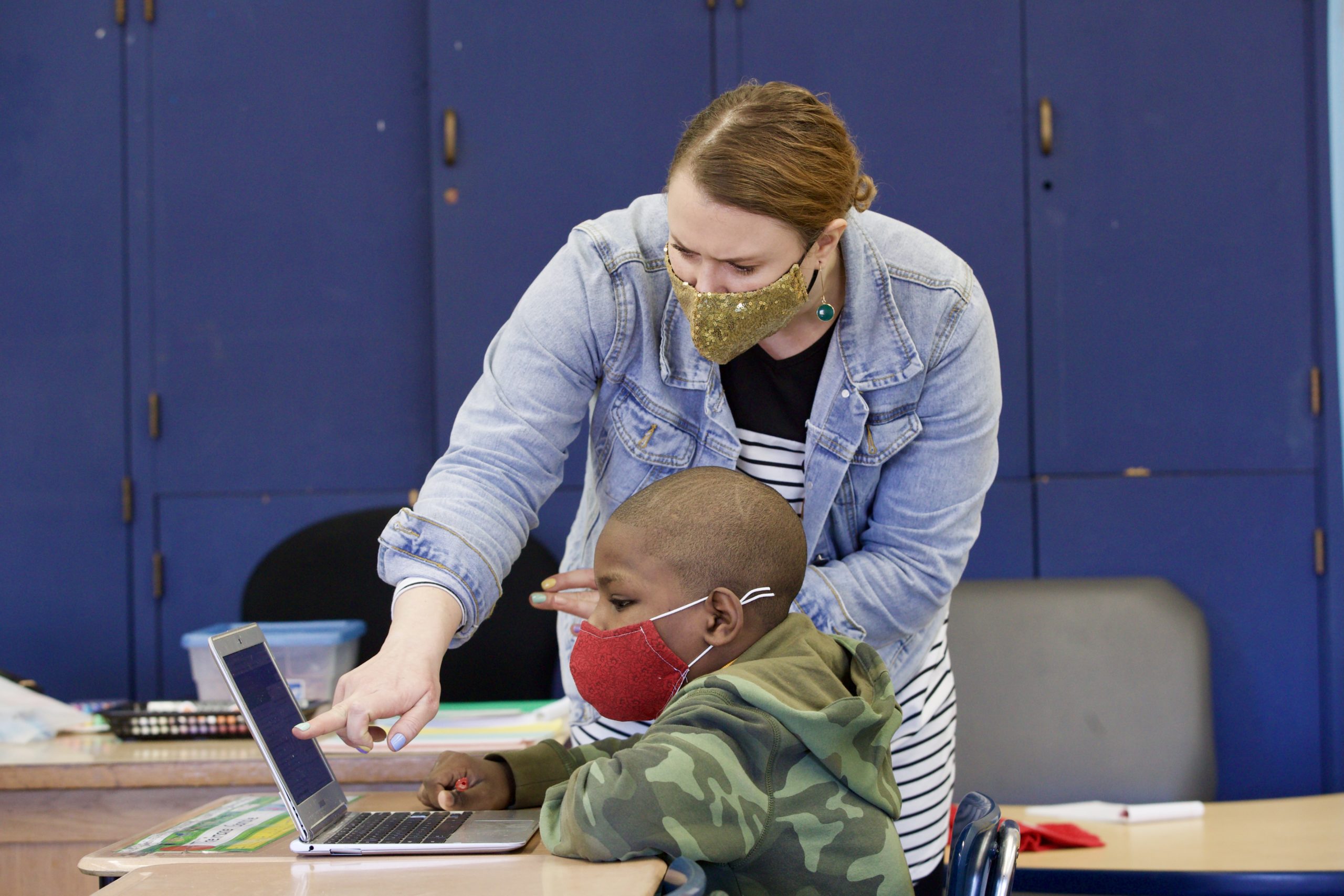 A teacher pointing to something on a student's laptop