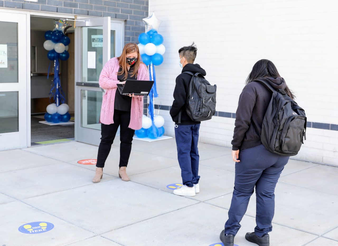 Teacher checking health screener before allowing students to enter school